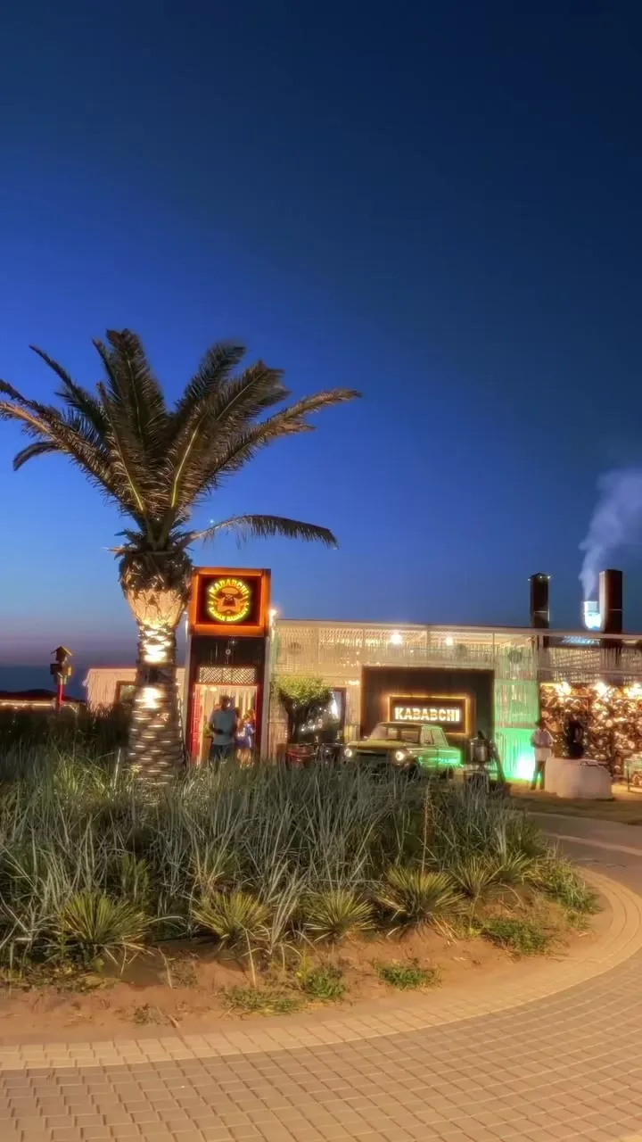 הכניסה בערב: השלט Kababchi, דקל והביתן המואר